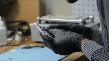 Adam atölyede bozuk akıllı telefonu tamir ediyor.