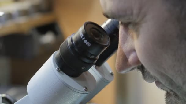 Mira a través del microscopio. El médico mira a través del microscopio. Un científico mira a través de un microscopio. El maestro en el centro de servicio mira en un microscopio — Vídeos de Stock