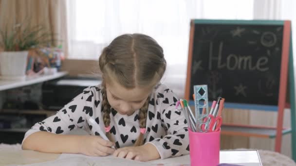Hermosa colegiala está sentada en la mesa. Haciendo deberes con mamá en casa . — Vídeos de Stock
