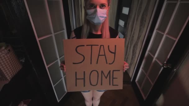 Frau mit Maske hält eine Botschaft an die Menschen in ihren Händen, zu Hause zu bleiben. Quarantäne — Stockvideo