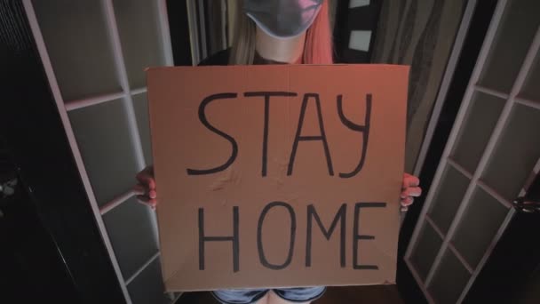 La mujer con una máscara sostiene una sábana con la inscripción permanecer en casa. Cuarentena . — Vídeos de Stock