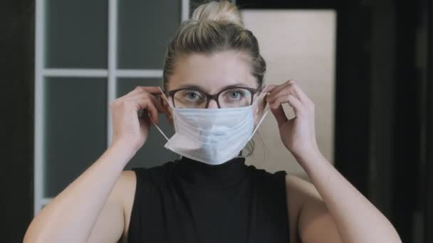 Mädchen, Frau setzt eine medizinische Schutzmaske auf und schaut in die Kamera. Coronavirus Quarantäne-Konzept. Die Frau ist eingesperrt. Quarantäne. Gesichtsmaske — Stockvideo
