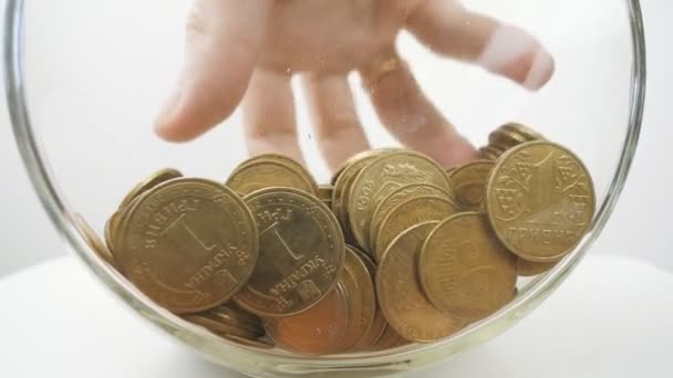 Monedas de metal en un frasco de vidrio, una mano está recogiendo monedas. Primer plano. Hryvnia . — Vídeos de Stock