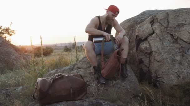 带着热水瓶的男性游客在石头上喝茶 停止休息的天性 — 图库视频影像