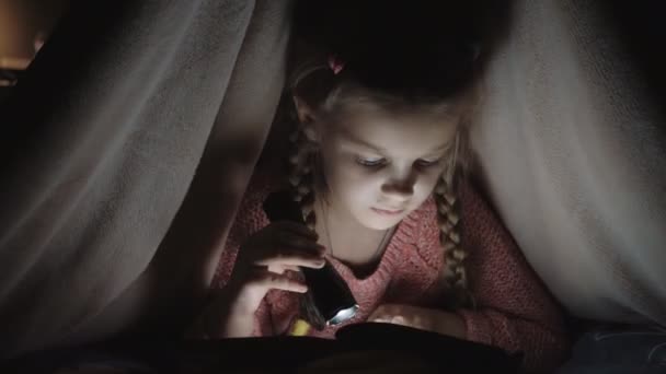 Dziewczyna czytająca książkę. Dziewczynka z latarką. Dziecko czyta w łóżku. — Wideo stockowe