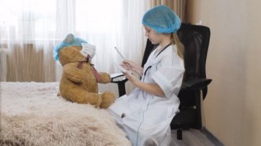 Evdeki hastanede oynuyorlar. Doktor kız hemşire deftere bir tanı koyuyor.