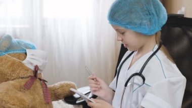 Evdeki hastahanede oynuyor. Veteriner doktor, hemşire deftere yazı yazıyor. Hastane ve ilaç. Küçük kız hastane oyunu oynarken beyaz üniforma giyiyor. Hemşire doktor hayali travmayı tedavi ediyormuş gibi yap..