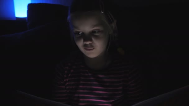 Fille avec un livre In Bedroom at Night. Kid Reading livre drôle Au lit. Joue à la maison. Petite fille mignonne avec un livre In Bedroom at Night. Enfant lecture drôle histoire au lit .
