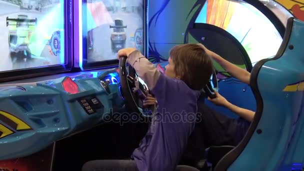 Мальчик играет в видеоаркадную игру на автосимуляторе — стоковое видео