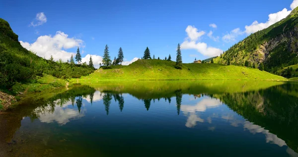 太陽の光と影の山の湖の海岸を対称的に澄んだ青い水に反映され ほぼシュールな風景を作成します — ストック写真