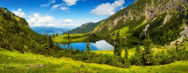 Gorgeous lake surrounded by mountains, the "Unterer Gaisalpsee" in the German Alps, with deep blue sunny sky reflected in the clear water and vibrant green meadows in the foreground