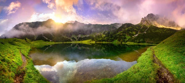 美丽的日出在阿尔卑斯山中的一个湖畔 群山环抱 五彩斑斓的云彩和薄雾映衬在清澈的水面上 穿过青草繁茂的小径上 — 图库照片