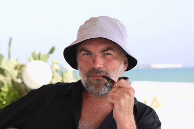 Sakallı adam deniz kıyısında pipo