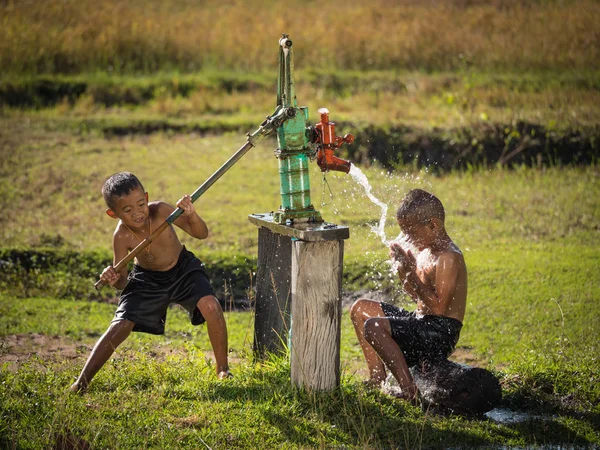Dois meninos balançando banhos de água subterrânea nos dias quentes . Fotos De Bancos De Imagens