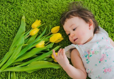 Çocuk çimlere çiçeklerle yatıyor.