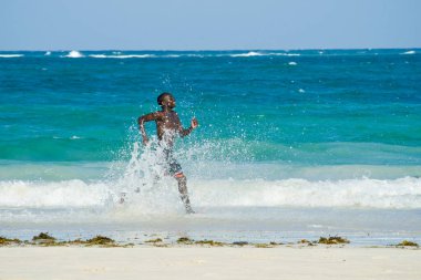 Mombasa. Kenya. 26 Ocak 2012 siyah adam okyanus kıyı çalışır ve dalgalar su sıçramalarına