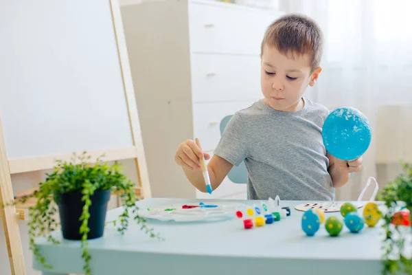 child paints eggs on wooden workpiece eggs sitting at table in a white room