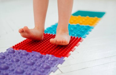 Bebek ayak masajı minderinde yeni yürümeye başlayan çocuk. Ortopedik masaj halısı üzerinde bacak egzersizleri. Düz taban ve halluks valgus önleme