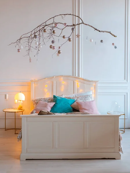 Chambre moderne confortable blanche avec décor festif. Lit en bois de style scandinave avec un bâton en bois dans un style minimaliste avec des boules étincelantes suspendues. — Photo