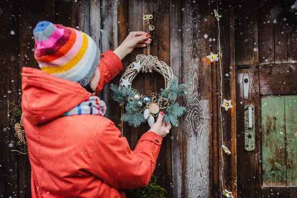 Вид сзади на молодых хипстеров украшает дом на Рождество у двери. Елочный венок на старом деревянном ржавом фоне. — стоковое фото