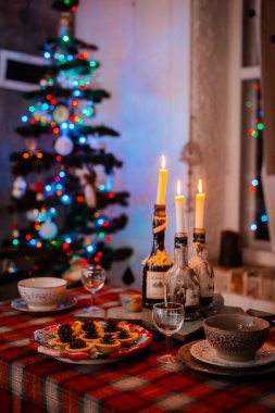 Geleneksel süslemeli Noel masası. Bokeh ışıklarının arka planındaki bir tabakta festival masası konilerinin yaratıcı dekorasyonu.