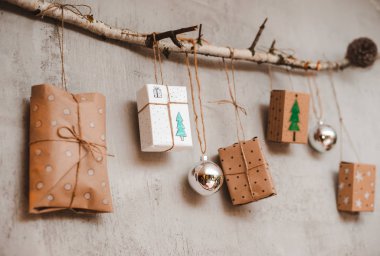 Kraft kağıdı ve el yapımı süslemelerle paketlenmiş Noel hediyeleri gri beton bir duvara bağlanmış bir ipe asılıdır..
