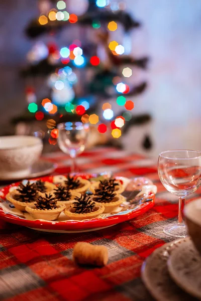 Hagyományosan díszített karácsonyi asztal. Kreatív dekoráció az ünnepi asztali kúpok egy tányéron a háttérben bokeh fények. — Stock Fotó