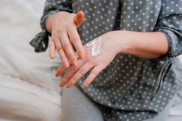 Feliz mujer madura saludable aplica una crema cosmética hidratante anti-envejecimiento en sus manos, sonríe a una señora de mediana edad con un cuidado suave y limpio de la piel y la belleza — Foto de Stock