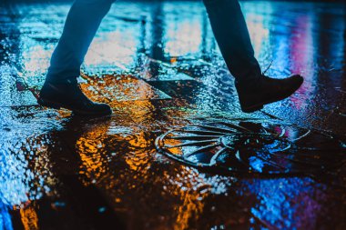 Büyük bir şehirde yağmurlu bir gece, ıslak yol yüzeyindeki renkli şehir ışıklarının yansıması. Yayaların cadde seviyesindeki manzarası. Soyut arkaplan. Odaklanamadı, alanın derinliği, bokeh