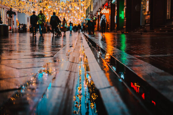 Rainy night in a big city, reflection of colorful city lights on the wet road surface. The view from the street level feet of pedestrians. abstract background. defocused, depth of field, bokeh