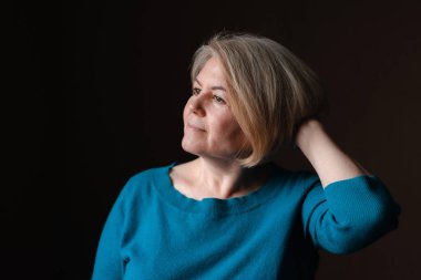 Evin koyu kahverengi arka planında açık renk saçlı, 50-60 yaşlarında, bakımlı, güzel, sarışın bir kadının portresi. yakın çekim, metin için boşluk