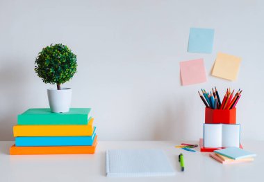 Renkli kâğıtlar, renkli kalemler ve beyaz duvar arkaplanındaki parlak kitaplarla öğrenci yaratıcı masaüstü düzeni. Okula dönelim. boş alan