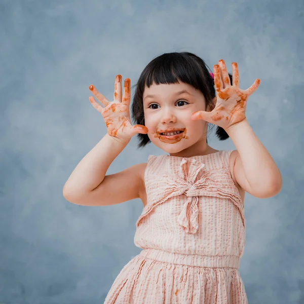 Küçük Kız Çikolata Yiyor Parmağını Gri Mavi Bir Stüdyoda Yalıyor — Stok fotoğraf