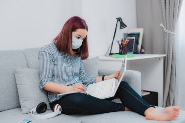 Genç liseli kız internet dersinde bilgisayarla virüs geçirmez maske takıyor, karantina sırasında sosyal uzaklık, internetten eğitim veren öğrenci koronavirüsü konsepti.