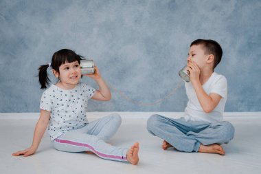 Genç bir erkek ve kız kardeş gri bir duvarın karşısında teneke bir telefonla konuşuyorlar. Çocuk iletişimi kavramı.