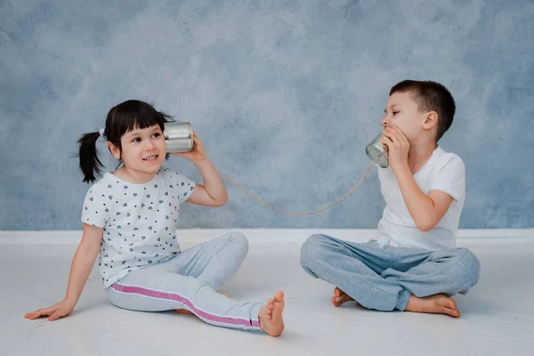 弟と妹が灰色の壁に向かってブリキの携帯電話と話している 子どものコミュニケーションの概念 — ストック写真