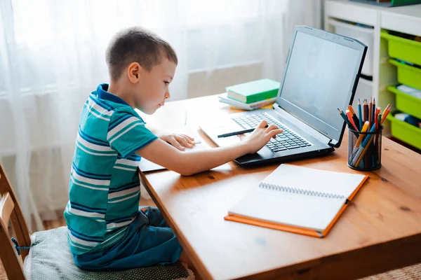 Educación a distancia en línea. Un colegial estudia en casa y hace los deberes escolares. Un hogar de aprendizaje a distancia — Foto de Stock