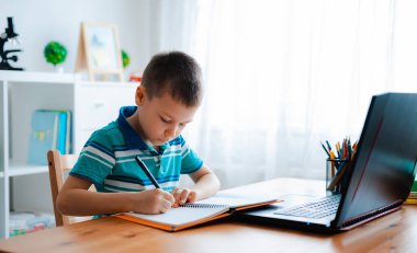 Distance learning online education. A schoolboy boy studies at home and does school homework. A home distance learning. clipart