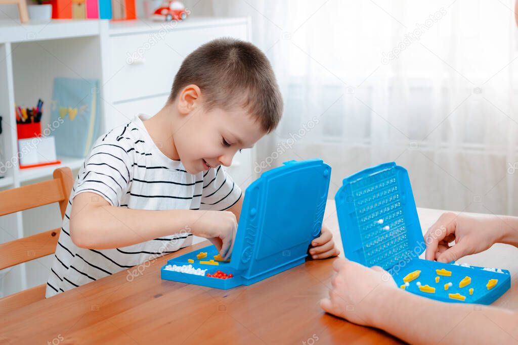 Boy child with dad playing warships and submarines are placed on the playing field in the game battleship. entertainment Board games at home in self-isolation in quarantine. Sea battle