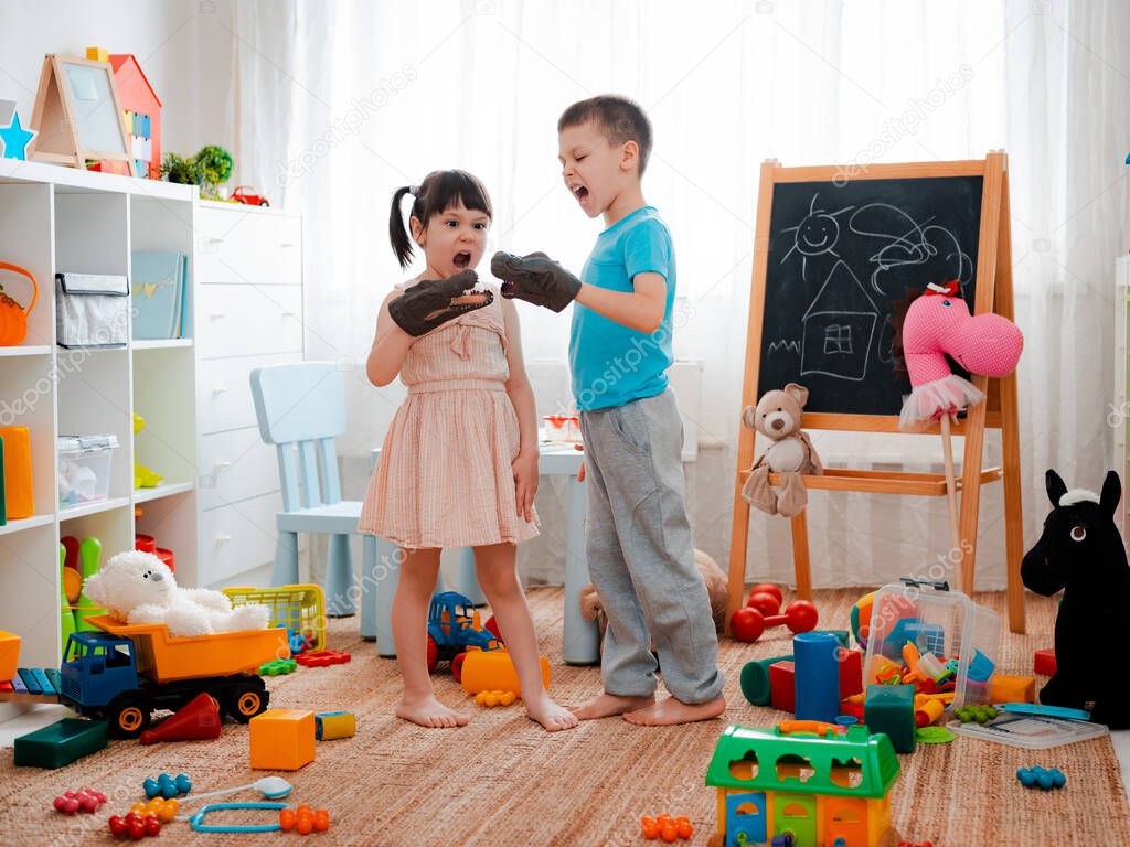 Boy and girl children scream toy dinosaurs noisily and play fun in the children's room. Children's self-expression and emotions during the game, mischief, toddler, chaos, brothers and sisters