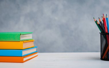 Bir yığın renkli ders kitabı ve gri-mavi arka planda parlak kalemler. Eğitim, eğitim, çalışma alanı, boş alan kavramı.