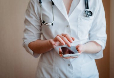 Kadın doktor elinde bir akıllı telefon tutuyor. Koronavirüs karantinası ve kendini izole etme konularında uzaktan tıbbi danışmanlık kavramı. Pratisyen hekiminle online istişare.