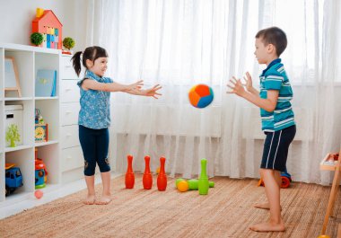 Yerli bir çocukla bir kız oyun odasında top oynuyorlar. Etkileşim konsepti, kardeşlik, iletişim, karşılıklı oyun, karantina, kendini tecrit evi, kardeş kardeş.