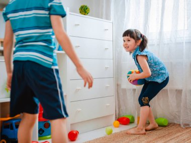 Yerli bir çocukla bir kız oyun odasında top oynuyorlar. Etkileşim konsepti, kardeşlik, iletişim, karşılıklı oyun, karantina, kendini tecrit evi, kardeş kardeş.