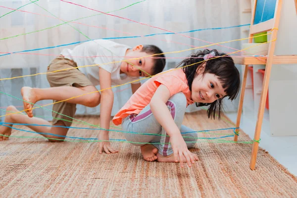小女孩的弟弟 兄弟姐妹 孩子们爬过绳子网 在室内探索游戏障碍 在家里主动玩耍 自我隔离的概念 — 图库照片