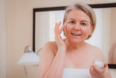 Yaşlı kadın gözlerinin altındaki siyah halkalara karşı yaşlanma önleyici losyon kullanıyor. Mutlu Olgun Kadın kırışıklıkları gizlemek için kozmetik kremi kullanıyor. Günlük nemlendirici kullanan bir kadın..