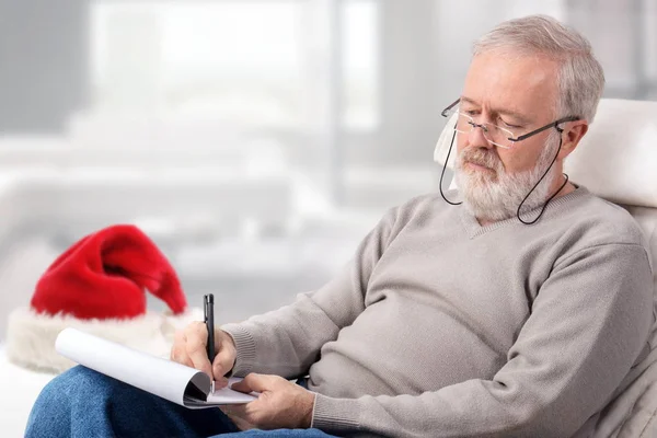 Man making the shopping list for holidays next to a red hat — Stock Photo, Image