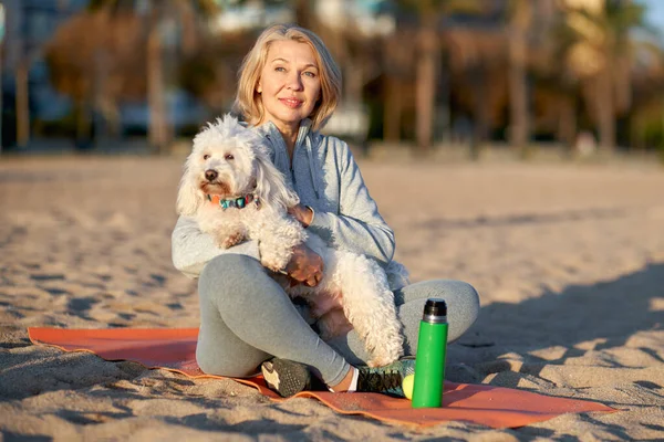 Femme adulte reposant sur la plage avec un chien blanc . — Photo