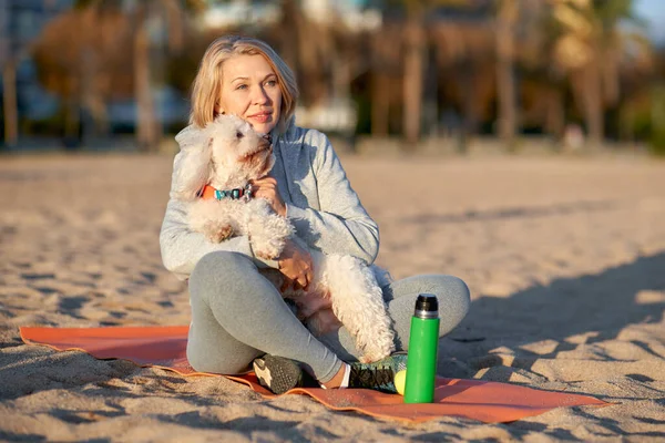 Adult woman resting on the beach with a white dog. — Stockfoto
