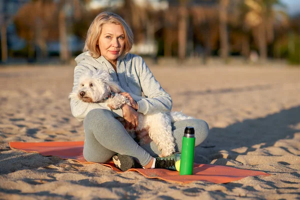 Elderly woman resting on the beach with a dog. — Stockfoto